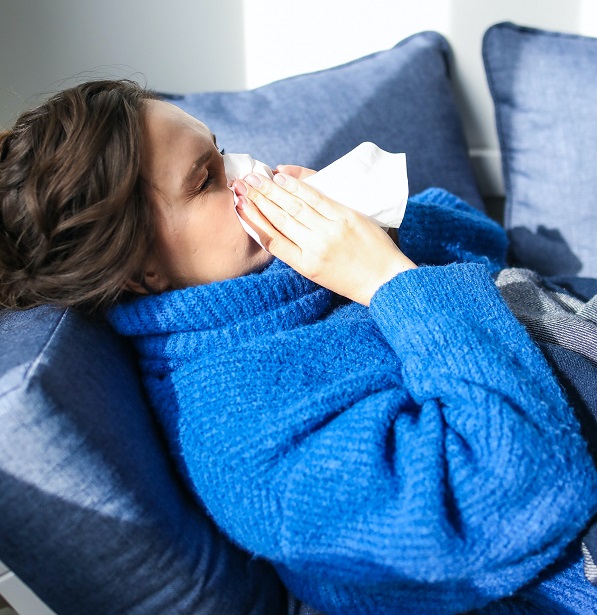 woman with tissue sneezing on couch