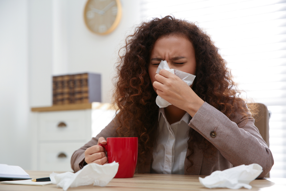 Woman who is sick sneezing into tissue.