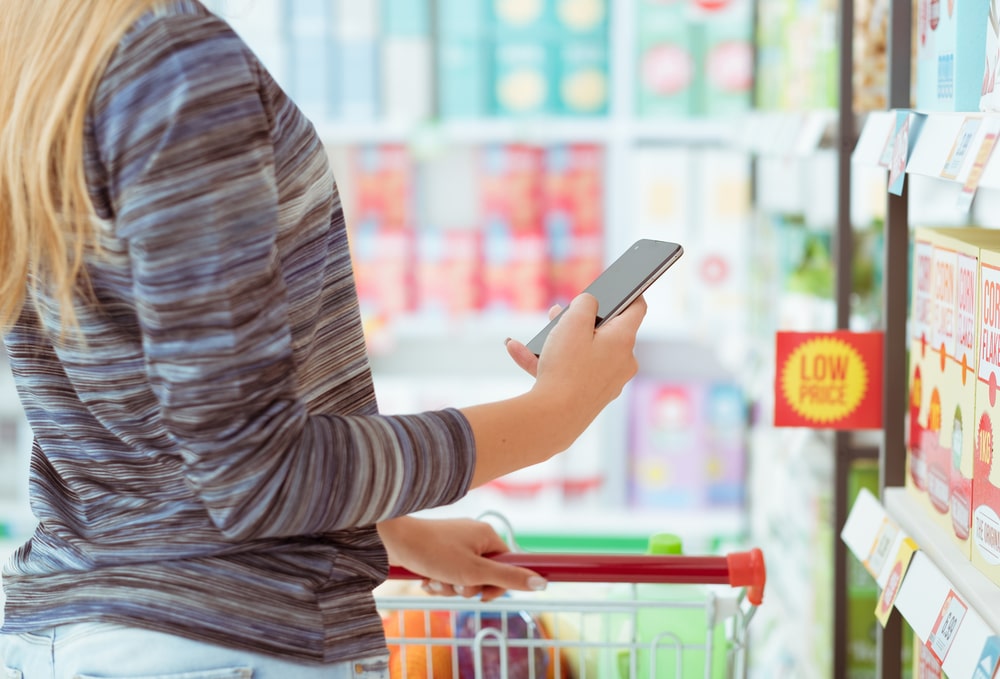 Woman doing grocery shopping at the supermarket, she is searching products and offers using apps on her phone